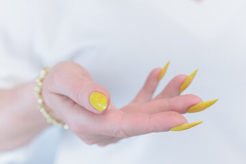Fototapeta premium Female hand with long nails and a bottle of bright yellow orange nail polish 
