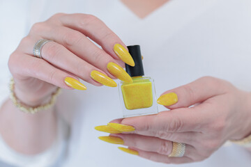 Female hand with long nails and a bottle of bright yellow orange nail polish	