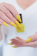 Female hand with long nails and a bottle of bright yellow orange nail polish	