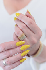 Female hand with long nails and a bottle of bright yellow orange nail polish	