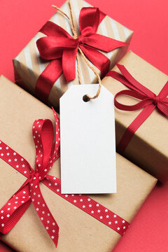 Blank gift tag mockup with twine attached, placed on beautifully wrapped gift boxes featuring red ribbons, ideal for holiday gifting and creative design projects with copy space