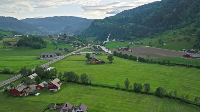 Aerial view of farmland near Steinsdalsfossen in Norheimsund, Norway. Drone footage showing green fields, scattered farmhouses, and valley landscape during summer.