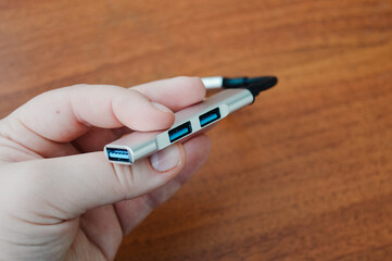 Hand holding a USB hub adapter with multiple ports on a wooden desk. Concepts: modern technology, data transfer, remote work, office accessories, connectivity.