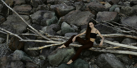 dried trunk. girl sits on dry fallen trees on which the girl sits in brown trousers black top....