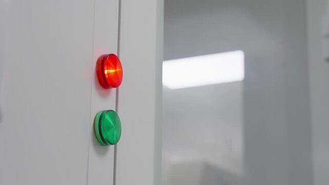 Close-up of an illuminated red indicator above a green button on a sleek industrial control panel, signaling operational status in a clean laboratory environment with reflective glass surfaces