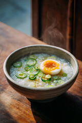 Bowl of congee with green onions and soy marinated egg in a ceramic bowl with rising steam on wooden table evoking gentle comfort and warmth  
