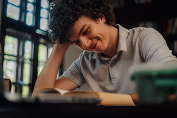 Young man smiling and reading a book in a library