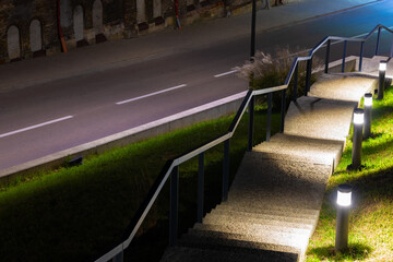 modern town city square downstairs foot path way along decorative lanterns urban illumination with asphalt road below night long exposure scene without people