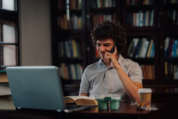 Student talking on phone while studying in library with laptop