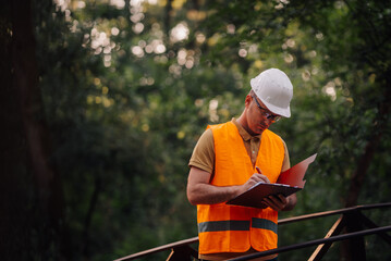 Construction engineer taking notes on a clipboard wearing an orange vest and white hardhat