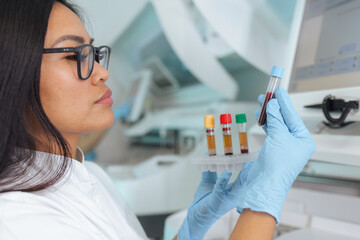 A professional Asian female scientist examines blood samples in a well-equipped pharmaceutical laboratory while performing clinical tests.