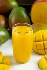 Glass of fresh mango juice surrounded by whole and sliced fruits. © Zarina Lukash