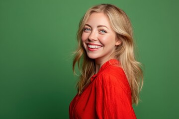 Smiling woman with blond hair in a vivid red shirt, looking over her shoulder against a green background. She exudes a cheerful and lively demeanor, with bright, confident eyes