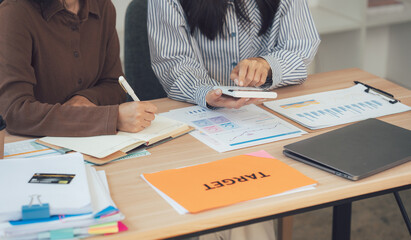 Businesswomen working together: Two businesswomen collaborate, focused on finances and strategy, their desks cluttered with financial documents and data.