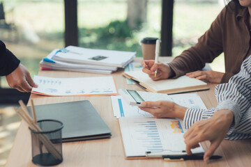 Strategic Partnership: Focused on a collaborative meeting, hands intently analyze reports, documents, and devices. Suggesting a moment of analytical discussion and a productive work dynamic.