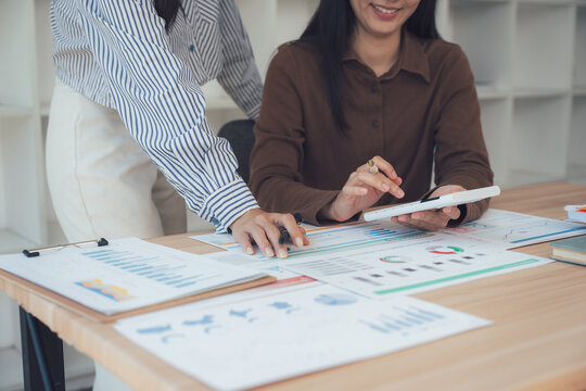 Collaboration & Analysis: Two businesswomen immersed in a collaborative environment, reviewing financial data on various charts, charts, and papers. - Powered by Adobe