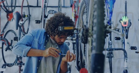 Tightening rear hub, denim-clad man leaning toward mounted rear wheel, using tool near drivetrain