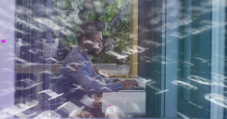 Typing man in blue denim shirt using laptop at window counter, alphanumeric reflections and planter