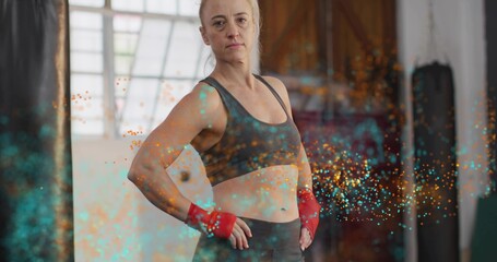 Posing woman in sportswear standing with red wraps at boxing gym big window with colorful particles