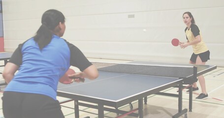 Leaning left player in blue shirt returning white ball at gym hall with table, net, paddles