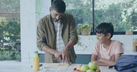 Cutting father slicing loaf on kitchen island, wearing olive overshirt, son in pink shirt watching
