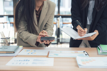 Analyzing Finances: Two businesswomen intently review financial data, meticulously calculating and documenting details to strategize a successful plan. 