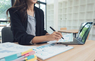 Office Analytics: A focused businesswoman, engrossed in a financial analysis, meticulously examines charts and graphs on her desk with laptop