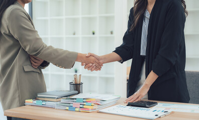 Handshake Agreement: Two businesswomen in a professional office setting seal a deal with a firm handshake, symbolizing partnership and a meeting of minds.