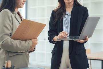 Collaboration and Strategy: Two professional women engaged in a focused business discussion, their attire exuding competence, as they collaborate with a laptop and documents.