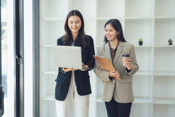 Dynamic Duo: Professional Women in Collaboration: Two elegant women, dressed in sharp business attire, engage in a productive discussion. One holds a laptop.