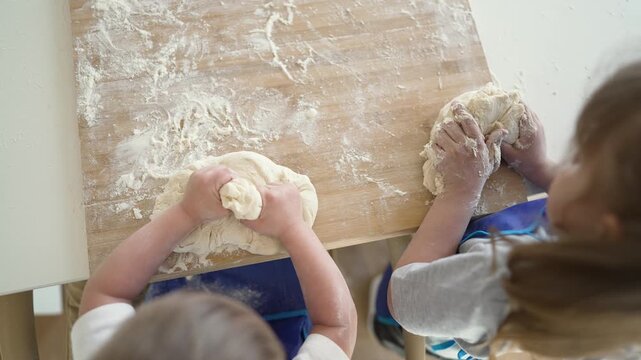 Knead dough on wooden table child uses hand and apron with flour during baking play in kitchen while child and hand press and shape dough covered with flour and crumbs and playful learning together