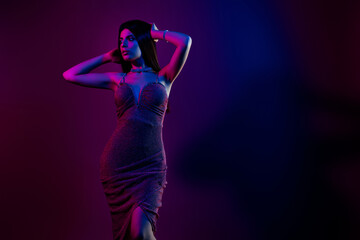 Passionate young woman in elegant dress posing under vibrant neon lights in stylish setting with...