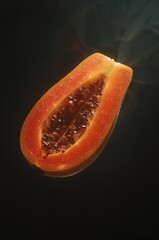 Glowing papaya half floats in darkness with radiant orange flesh and sparkling seeds