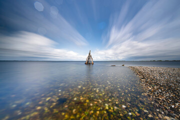 Majestic clouds dance over tranquil waters as sculptures stand sentinel near shoreline