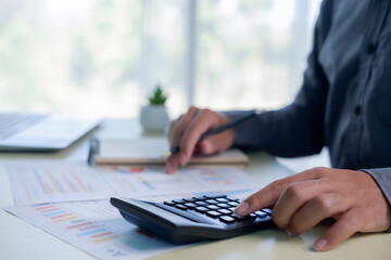 Hands using a calculator with financial charts and documents on desk, symbolizing budgeting, financial analysis, accounting, expense planning, business finance, investment review, money management.