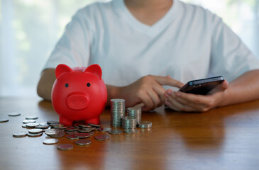 Personal savings and digital finance concept with red piggy bank, stacked coins and hand using smartphone, showing smart budgeting, mobile banking, money management and financial planning.