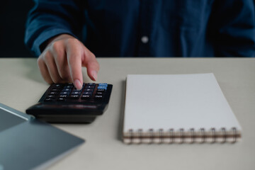 Person pressing calculator keys beside blank notebook on desk, personal finance planning and budgeting concept, expense calculation, saving money, financial management for home and business.
