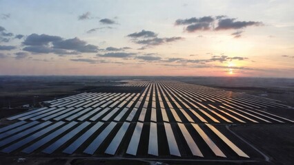 Aerial wide shot of a massive solar panel farm stretching to the horizon at sunset. Rows of photovoltaic panels reflect the golden light of the sun under a picturesque sky, representing renewable ener