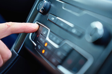 Close up of hand pressing button on car climate control panel to increase temperature during winter day. Concept of vehicle climate adjustment, driving comfort in cold weather