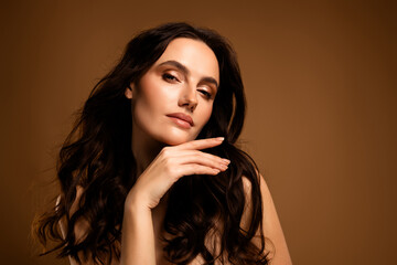 Charming woman posing confidently with flawless makeup and stylish hairstyle against a beige...