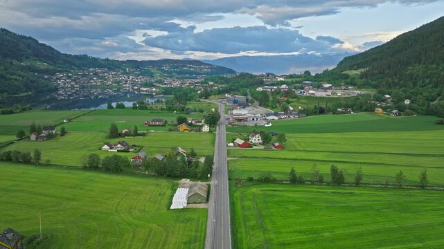 Aerial view of farmland near Steinsdalsfossen in Norheimsund, Norway. Drone footage showing green fields, scattered houses, and a straight rural road in the waterfall valley during summer.