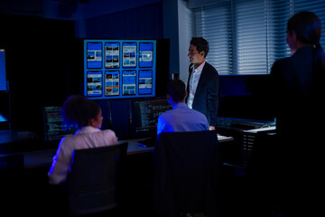 Corporate executive team brainstorming a business strategy in a modern high-tech office. Professionals discussing marketing concepts written on a transparent board while using digital devices.