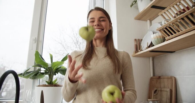Playful happy woman juggling green apples in the kitchen