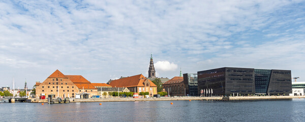 Historic brick buildings along a calm waterfront with modern black museum and church tower