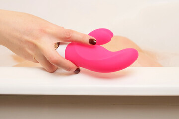 A woman takes a vibrator from the side of the bathroom while taking a bath