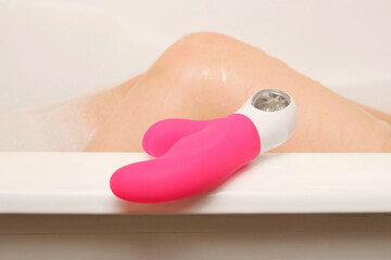 Pink curved vibrator resting on the edge of a bathtub