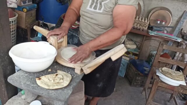 Traditional woman cooking handmade corn tortillas on a rustic wood-fired stove made from a metal barrel.