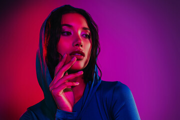 Young stylish woman posing in colorful neon lighting wearing hooded outfit, embracing modern urban...
