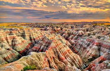 Big Badlands Overlook stands in Badlands National Park, South Dakota, USA. Scenic view features colorful eroded rock formations and sedimentary layers under a cloudy sunset sky