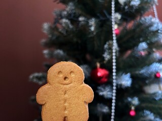 Gingerbread cookie shaped as a man placed in front of a decorated Christmas tree creates a festive holiday atmosphere.